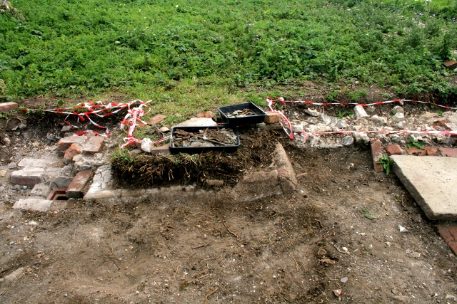 Looking S at concrete drain/gully in front of house between front door and woodstore