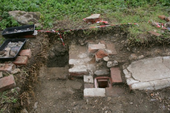Looking S from 'woodstore' doorway at ceramic drain and concrete gully outside kitchen/washhouse