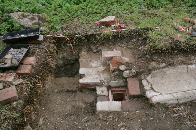 Looking S from 'woodstore' doorway at ceramic drain and concrete gully outside kitchen/washhouse