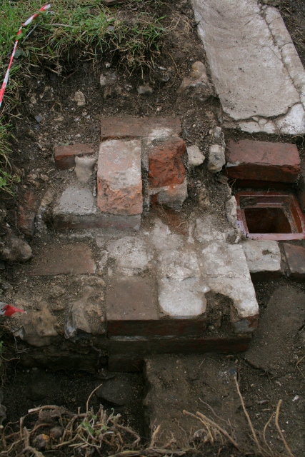 Looking W from 'woodstore' doorway at ceramic drain and concrete gully outside kitchen/washhouse