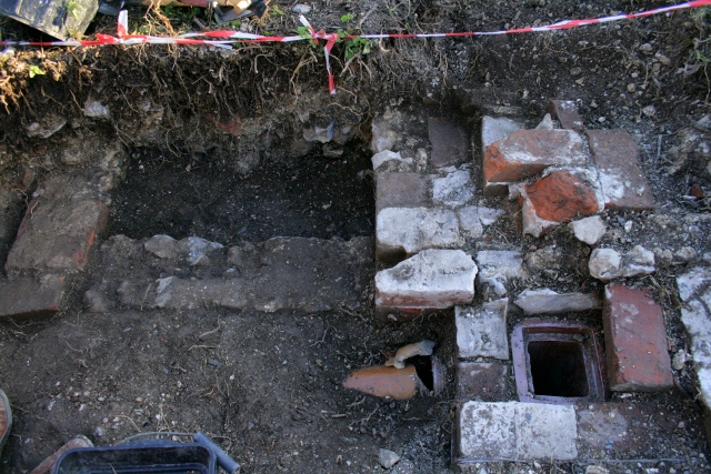 Looking S at gully trap and drain in front of NE corner of house and the 'woodstore'