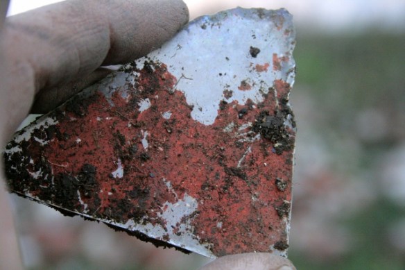 Reverse of mirror showing outer surface of anti-corrosion red-lead paint over reflective silver metal