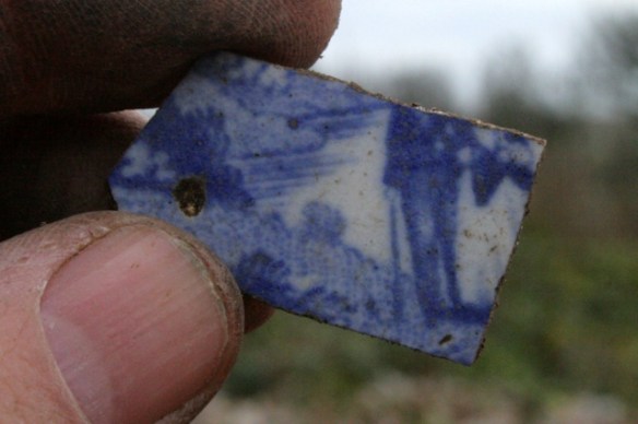 Blue and white ceramic shard of gentleman and lady in front of a pond or lake
