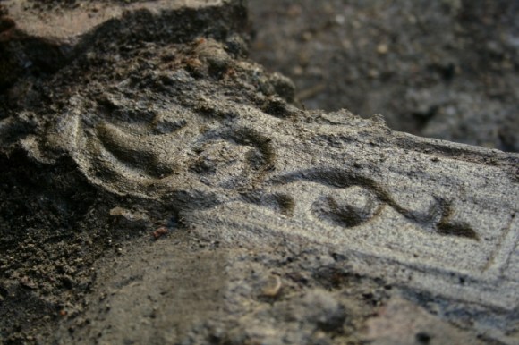 Part of a cast iron fireback embedded in masonry near base of demolition rubble near base of chimney