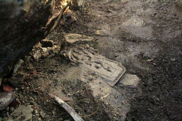 Part of a cast iron fireback embedded in masonry near base of demolition rubble near base of chimney