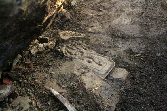 Part of a cast iron fireback embedded in masonry near base of demolition rubble near base of chimney