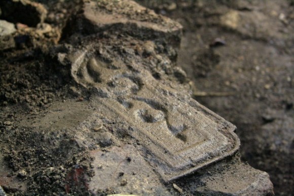 Part of a cast iron fireback embedded in masonry near base of demolition rubble near base of chimney