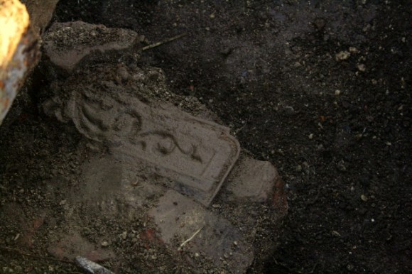 Part of a cast iron fireback embedded in masonry near base of demolition rubble near chimney base