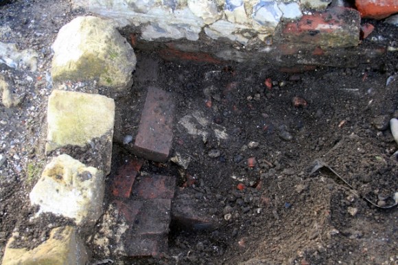 Looking W at sondage between E side of outside toilet & edging stones to N of path