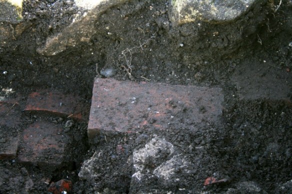Looking S from E of outside toilet at sondage below 1940's ground surface, at foot of N side of edging stones to path
